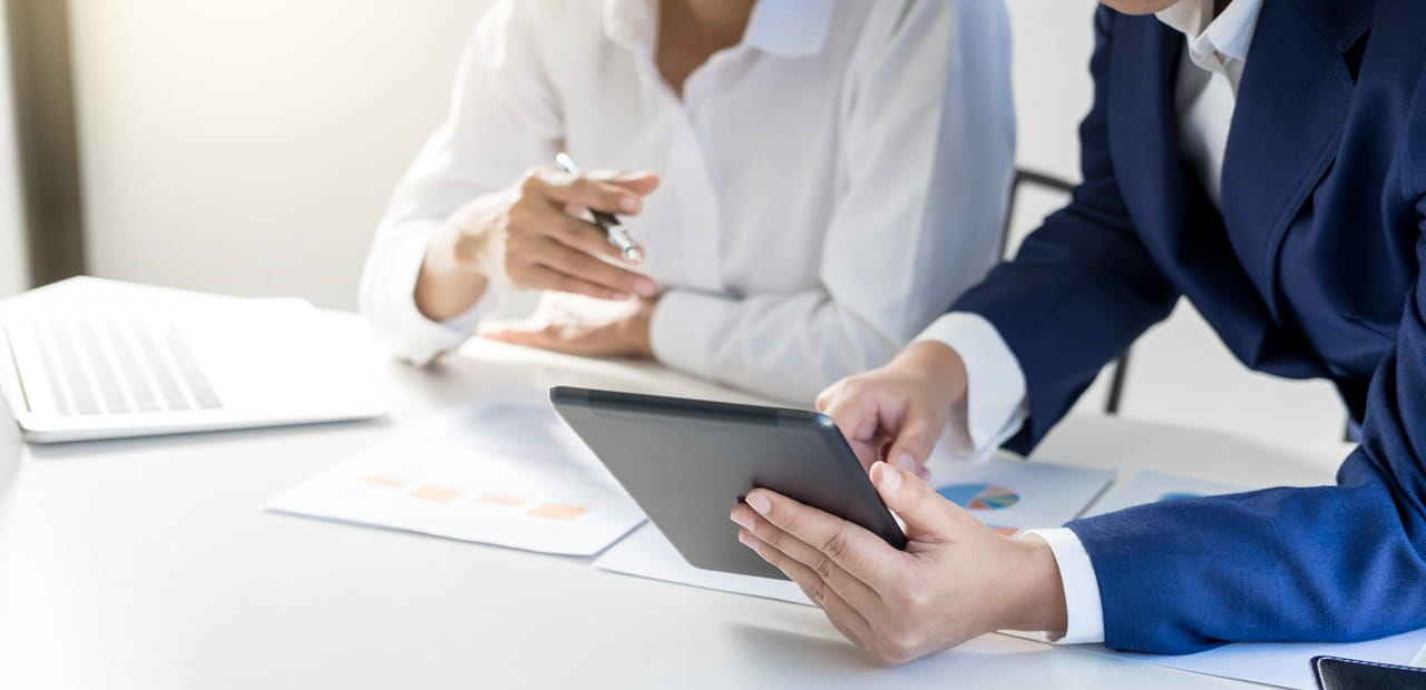 Two professionals' hands looking at a tablet while reviewing documents  at a conferenced table/