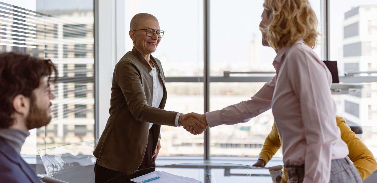 Businesswomen standing and shaking hands across a conference table.