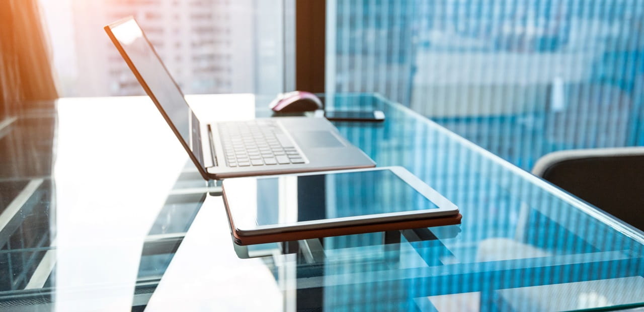 Tablet and laptop sit on a glass table