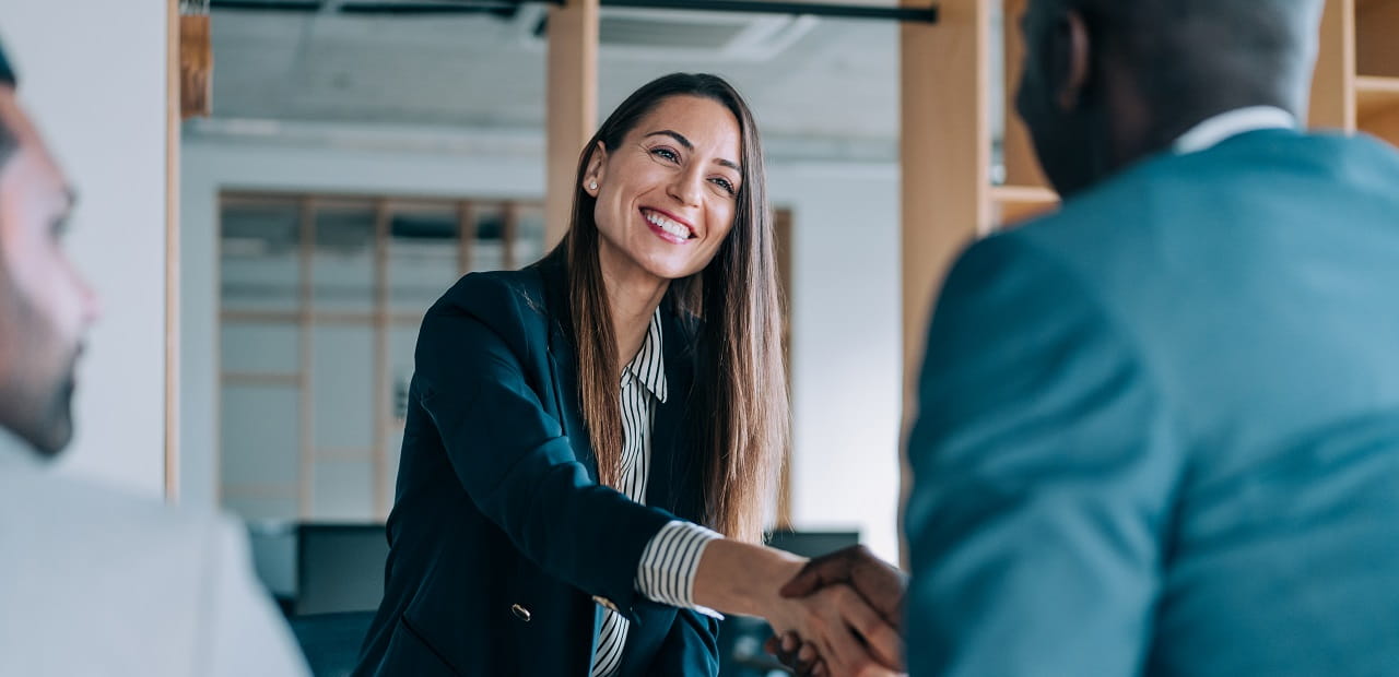 A professional woman shakes hands with another business man in an office setting.