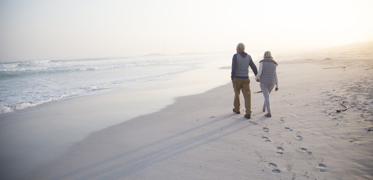 Rearview of retired couple walking on the beach.